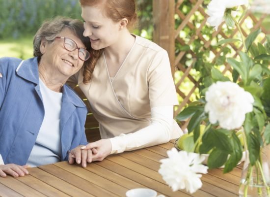 Happy grandmother enjoying time with friendly nurse on the terrace of sanatorium